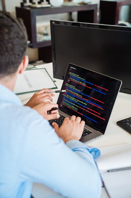 An indoor scene displaying a computer screen filled with programming code in various colours, including HTML tags and image links, set against a dark background. The code features highlighted syntax i